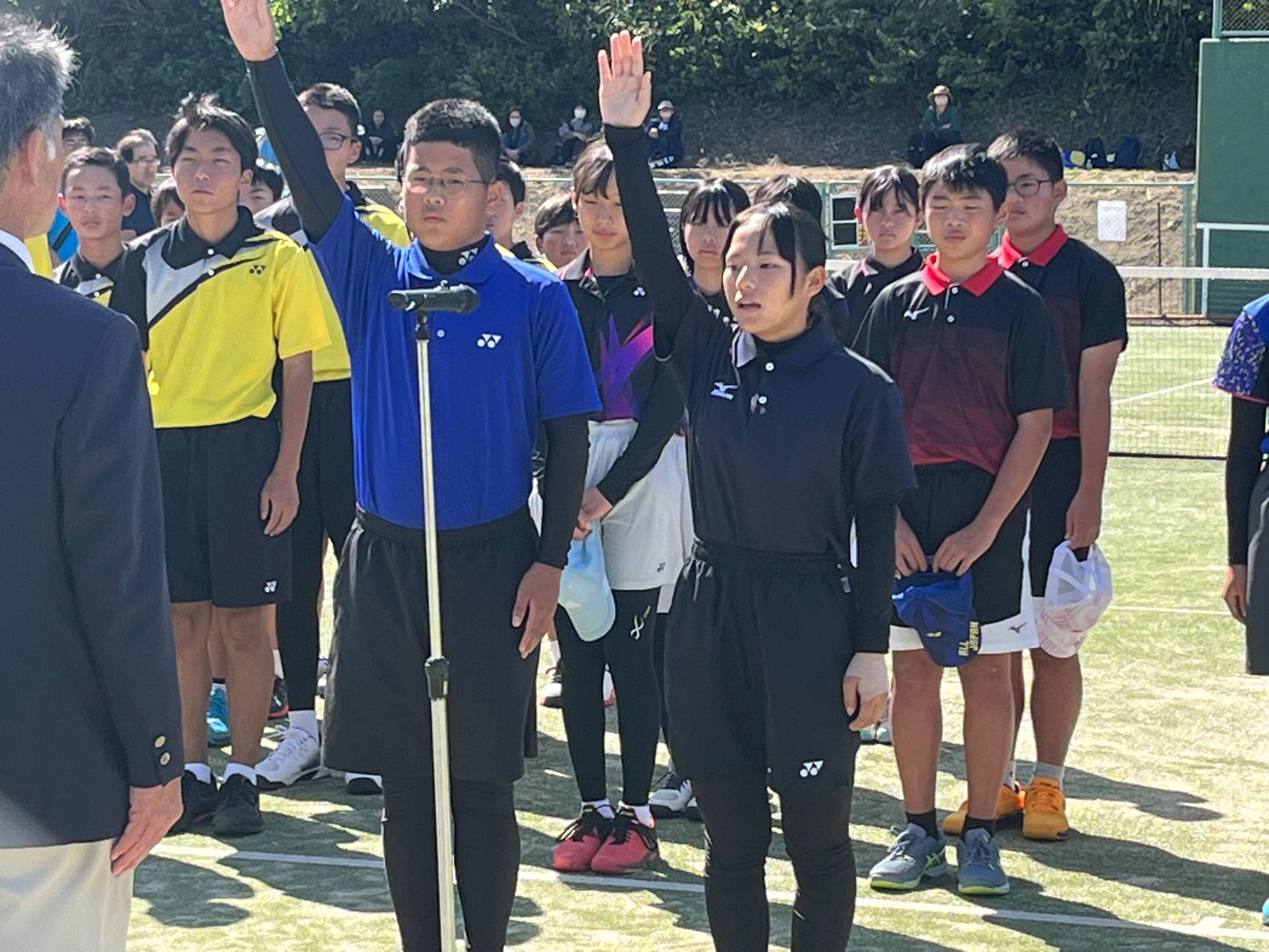 テニスコートで選手宣誓をする男女の写真