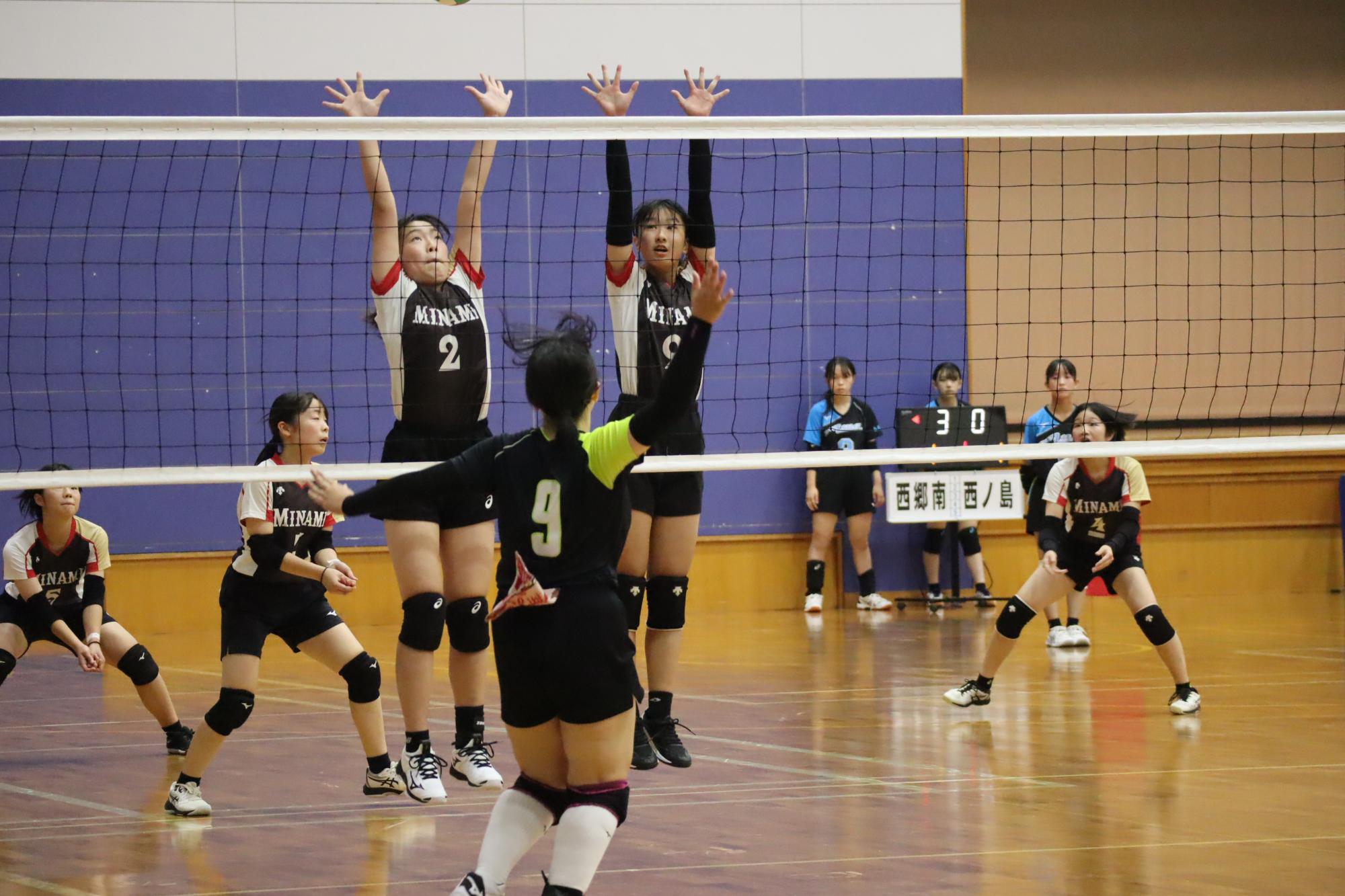 体育館のコートで女子生徒たちがバレーボールの試合をしている写真