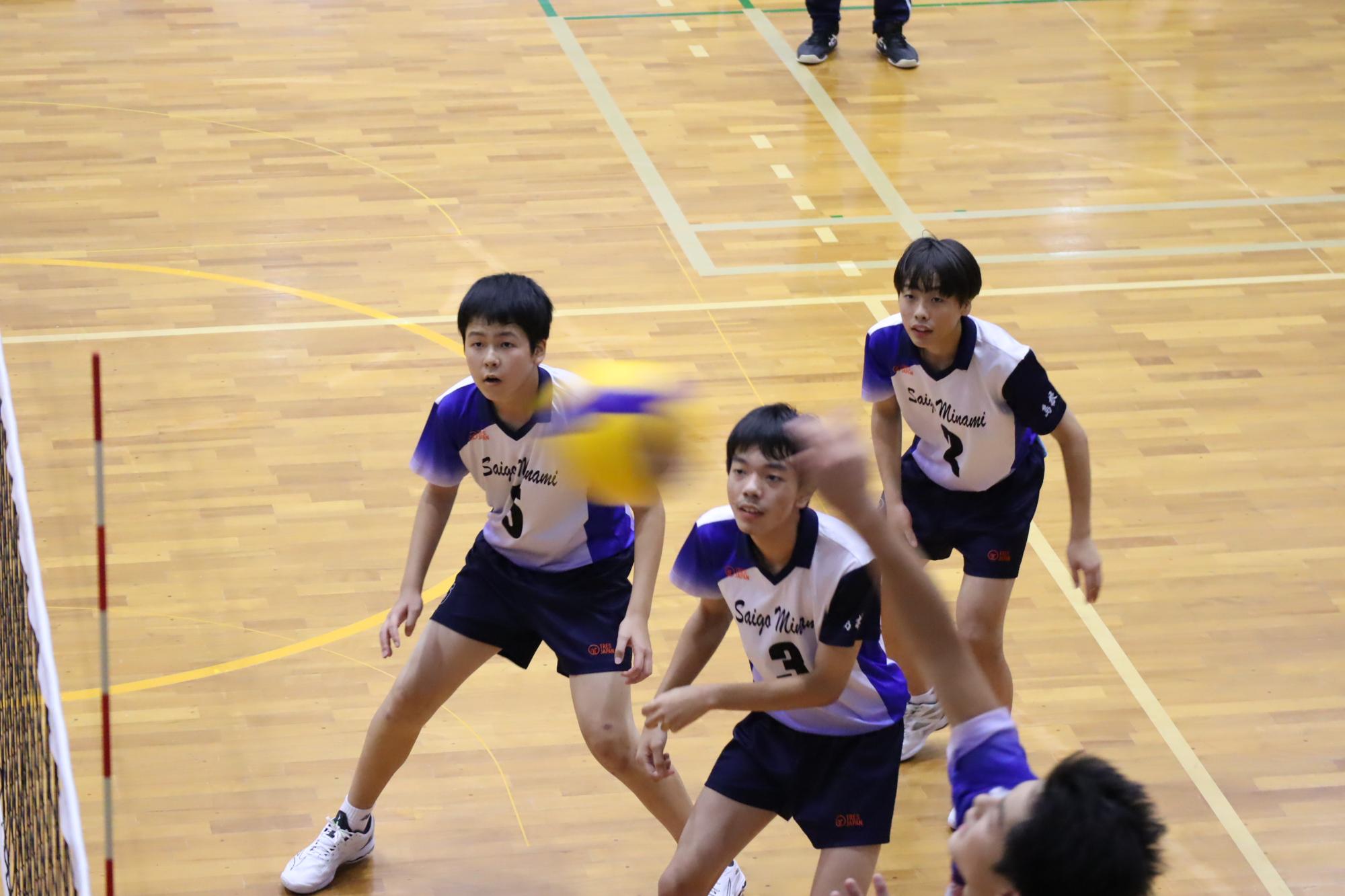 体育館のコートで男子生徒たちがバレーボールの試合をしている写真