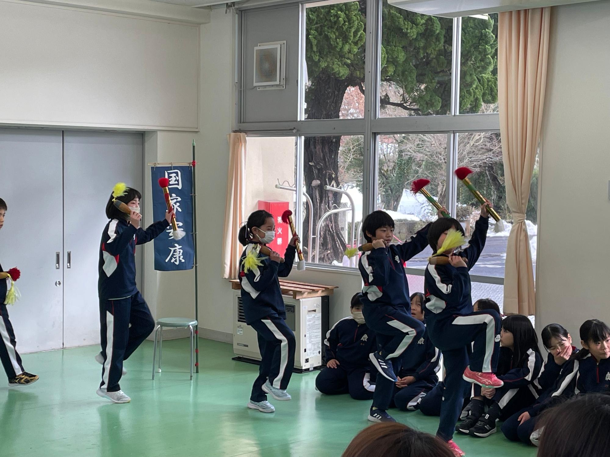 教室で児童たちが小道具を手に踊りを披露している場面の写真