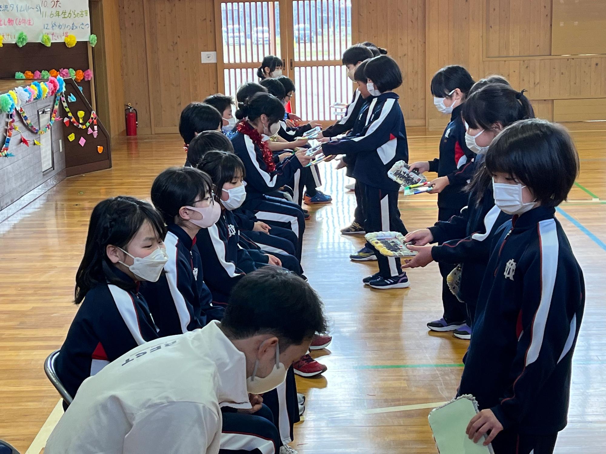 体育館で児童たちが列になって向かい合いプレゼントを手渡している写真