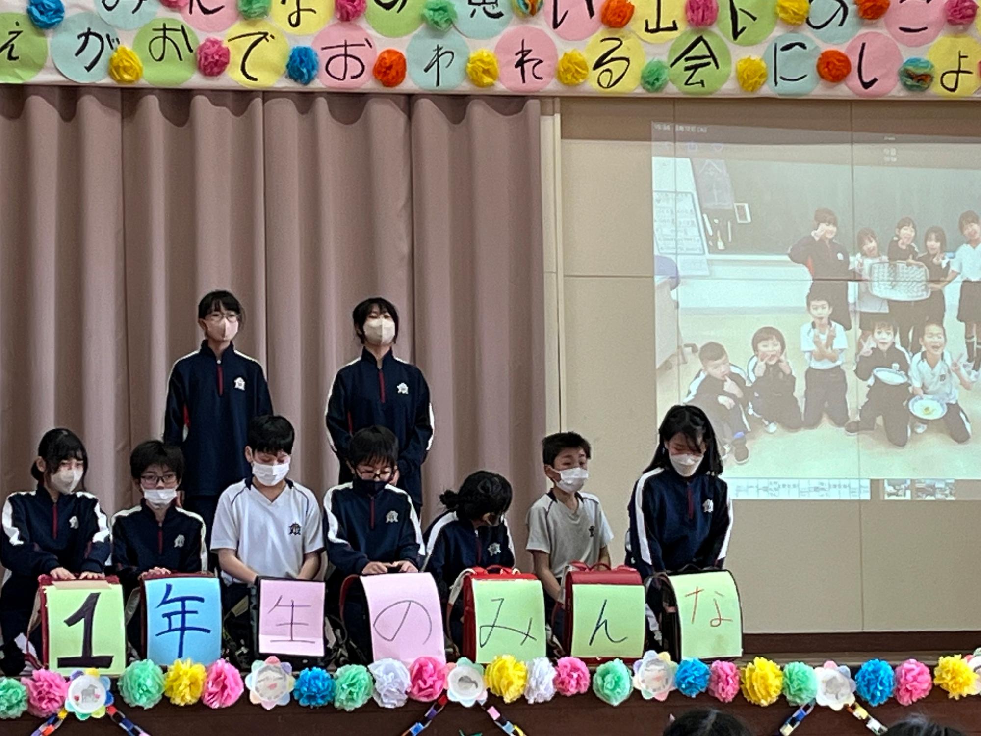 体育館の舞台上で上級生がスクリーンに写真を映しながら一年生に向けて発表している写真