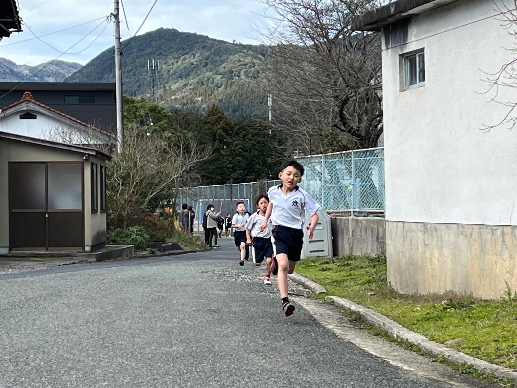 学校近くの道路で先頭の児童を中心に仲間が続いて走っている写真