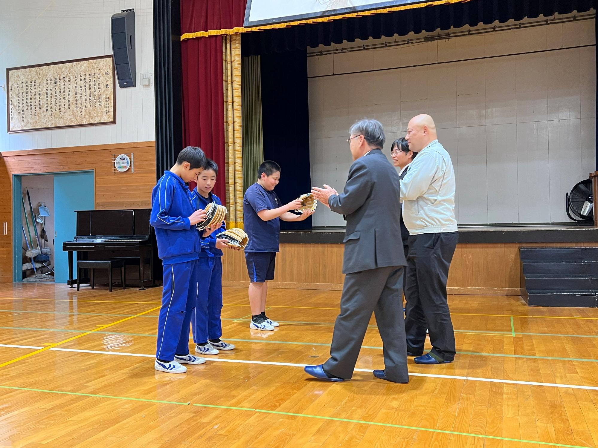 体育館で児童が先生から記念品を受け取っている写真