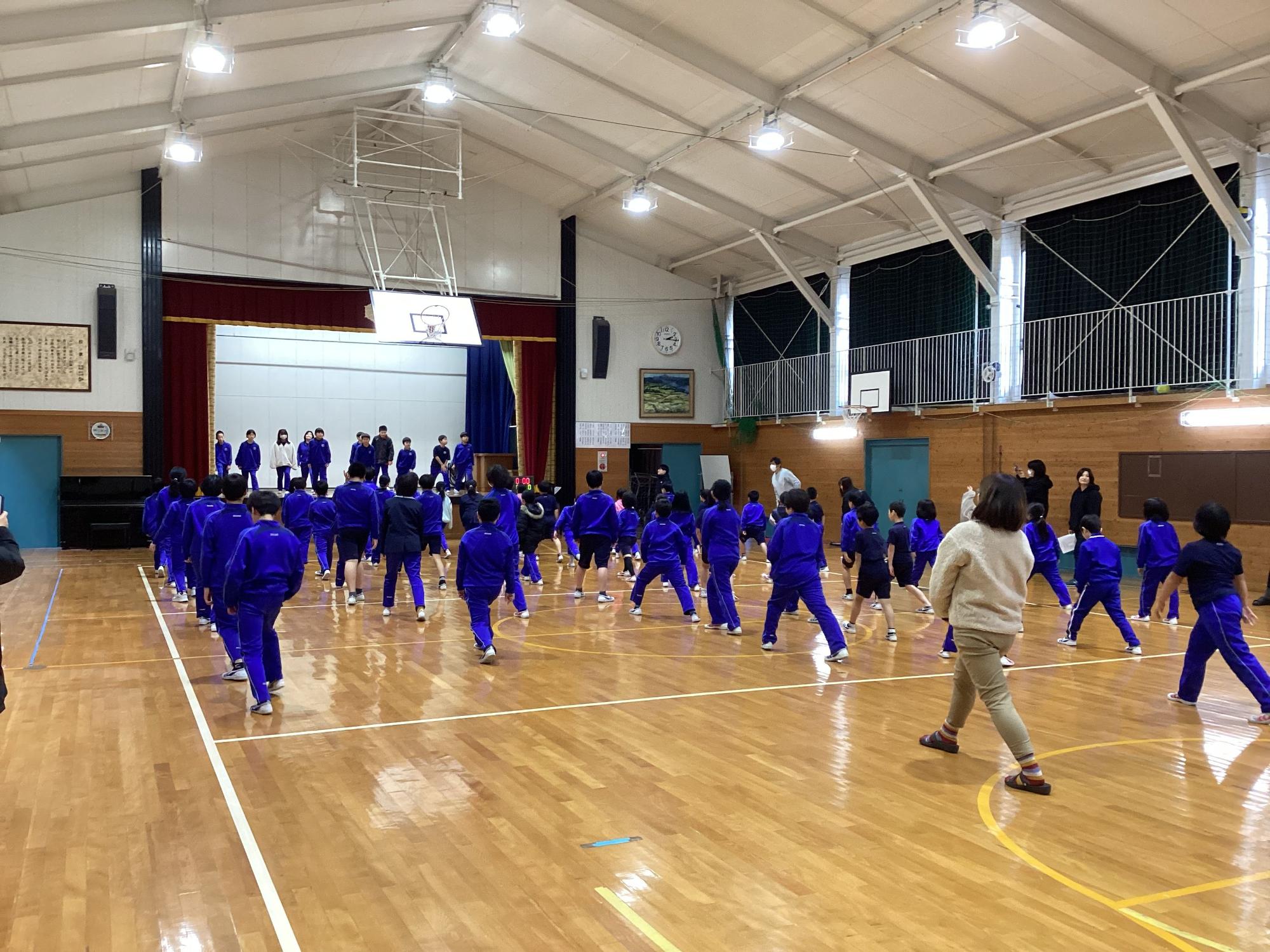 体育館で児童がステージに立つ友達に合わせて体を動かしている写真