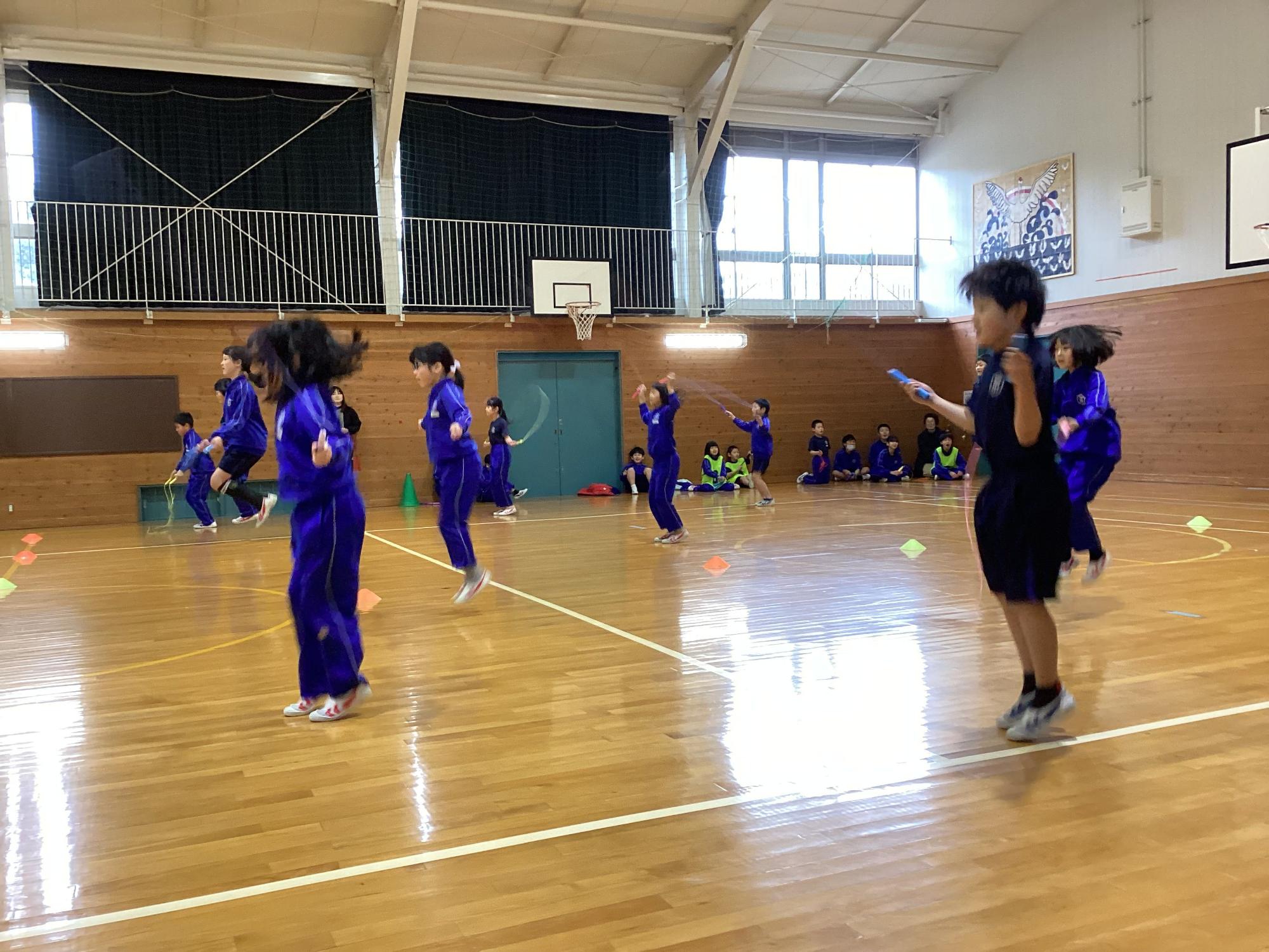 体育館で複数人の児童たちがなわとびをしている写真