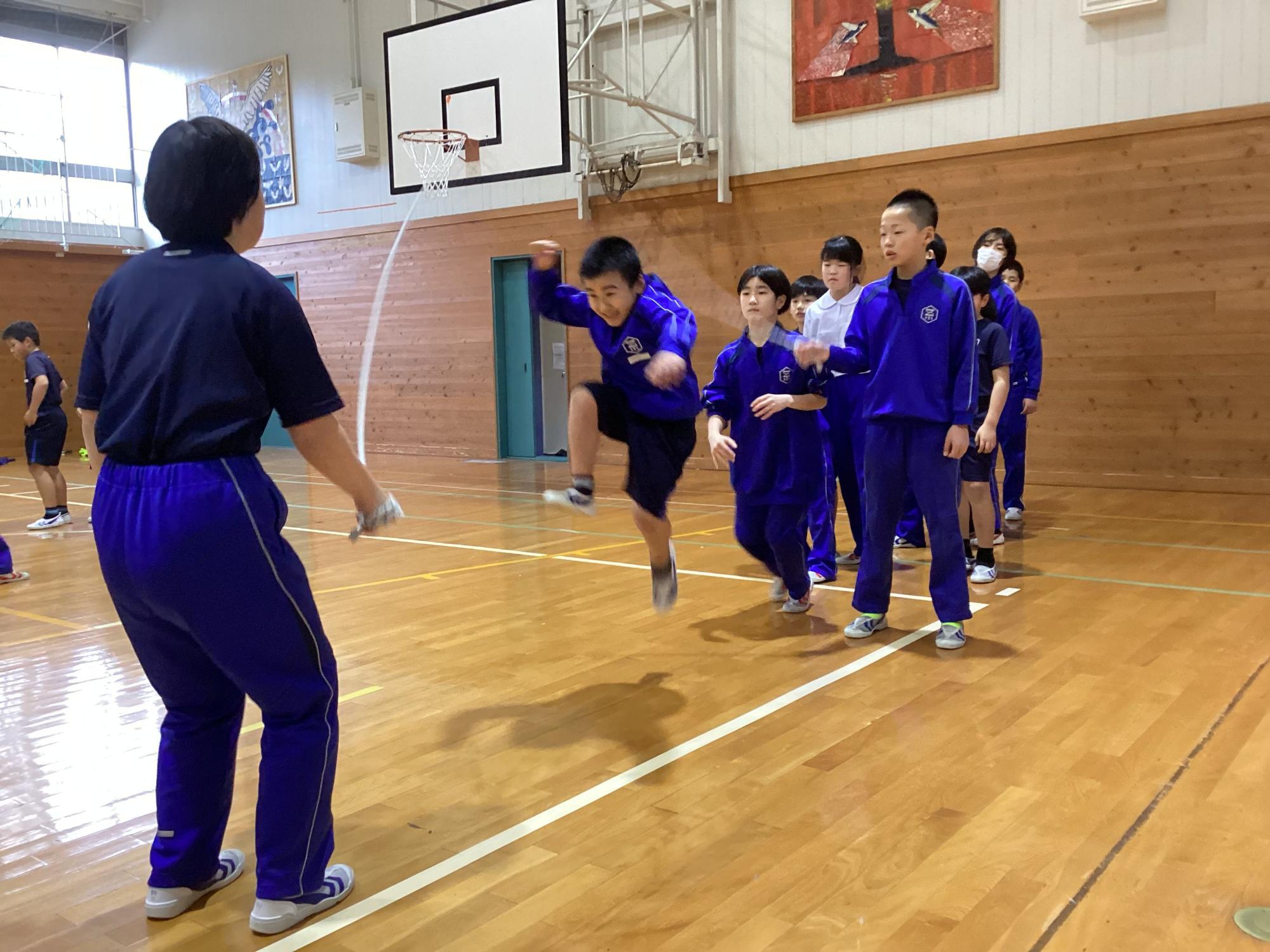 体育館で複数人の児童たちが大縄跳びをしている写真