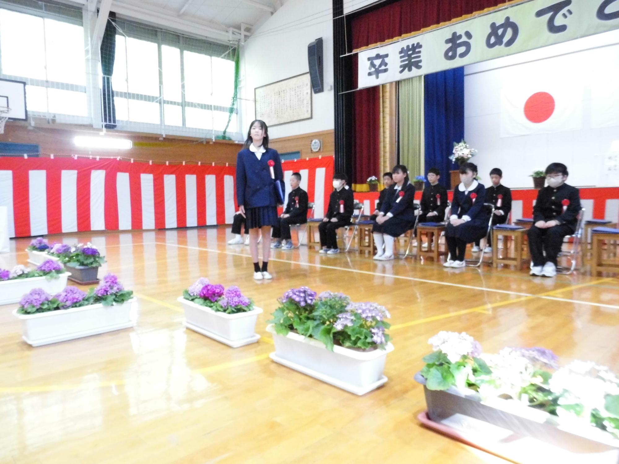 卒業おめでとうの垂れ幕の下で卒業式に臨む生徒たちの写真