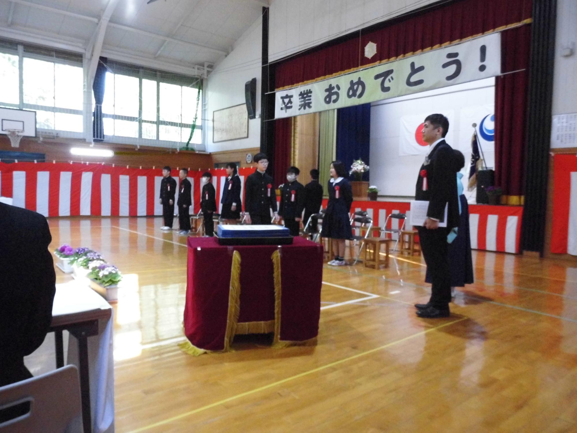 卒業おめでとうの垂れ幕の下で卒業生が証書を持って並んでいる写真