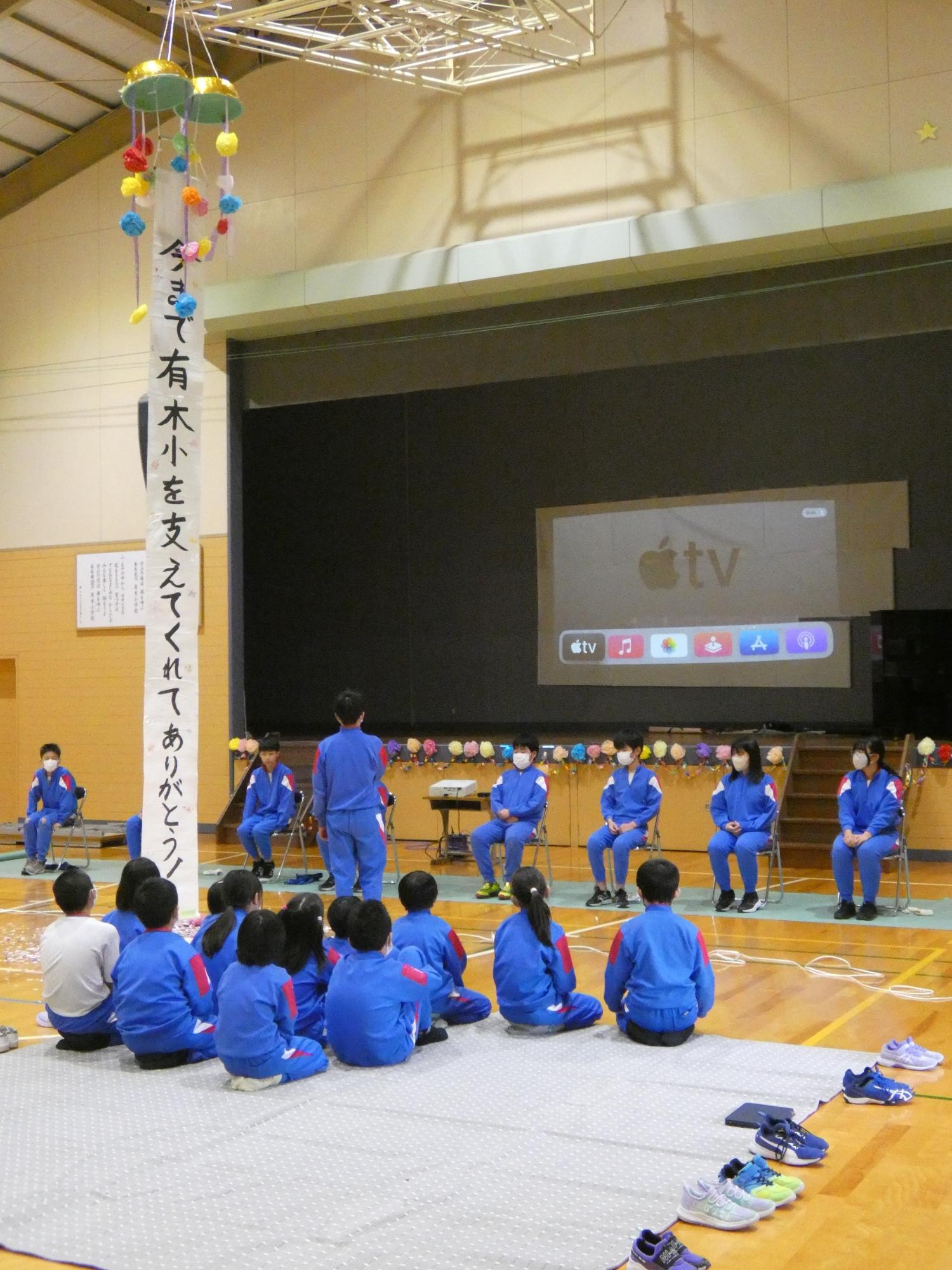 体育館で児童たちが卒業を祝う会を開いている写真