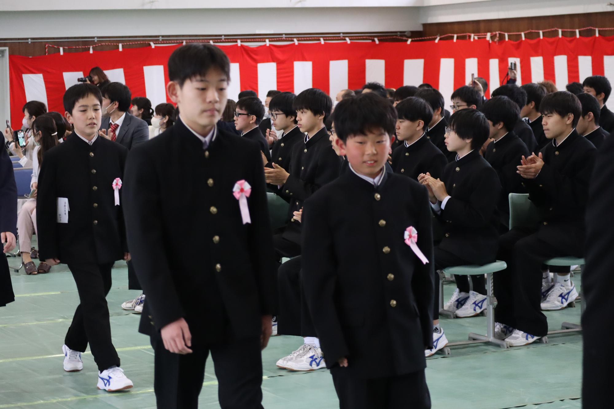 体育館で新入生の男子生徒たちが入場している写真