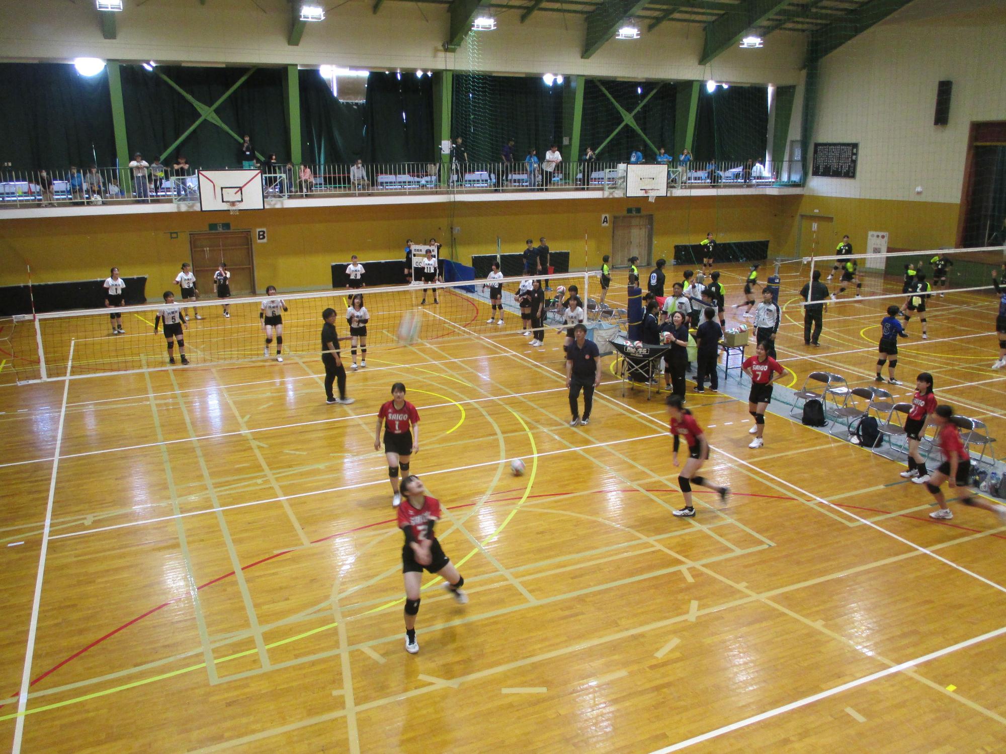 体育館でユニフォームを着た生徒たちがバレーボールの試合をしている写真