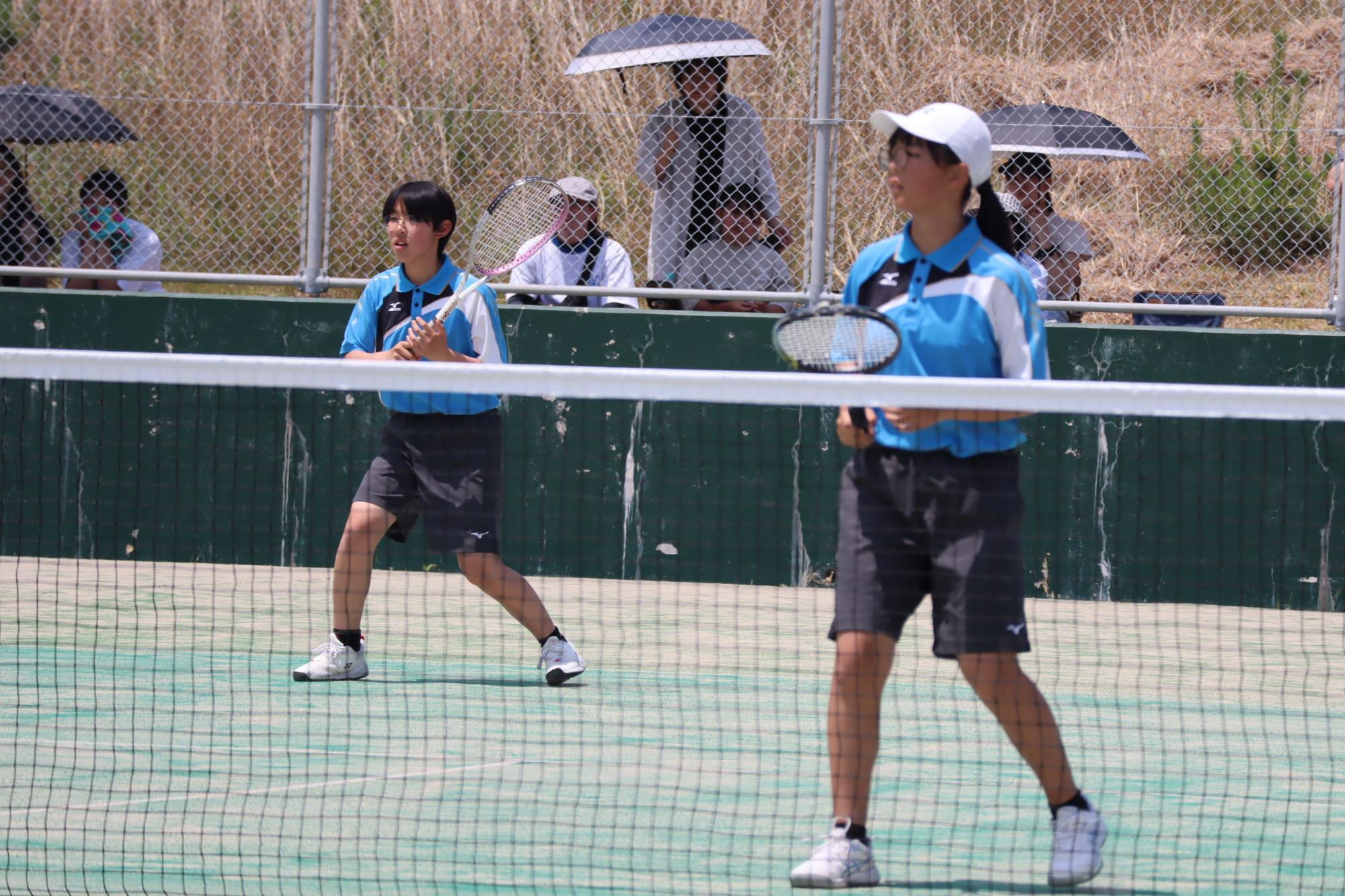 テニスコートで女子生徒たちがダブルスの試合に臨んでいる写真