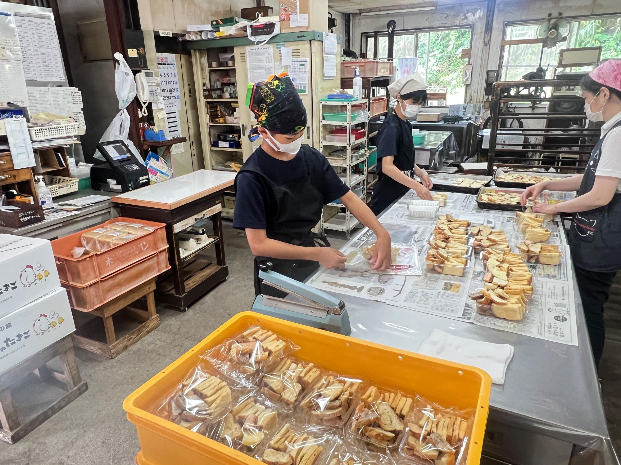 パン工房でエプロンを着けた生徒たちが焼き菓子を袋詰めしている写真