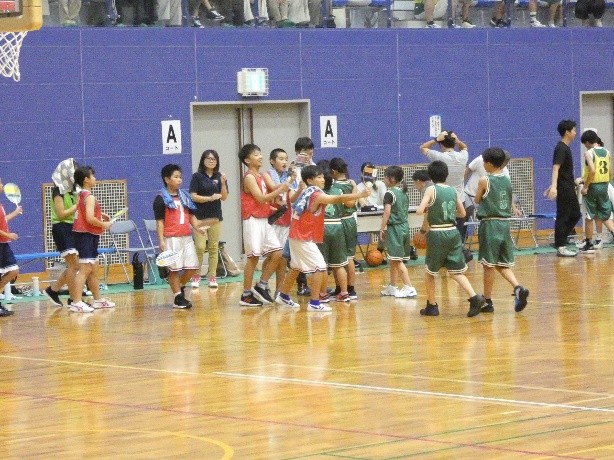 バスケットボール試合後に赤いチームの児童たちと緑のチームの児童たちがコートで集まっている写真