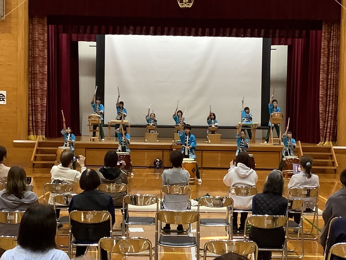 体育館の舞台上で児童たちが和太鼓を演奏している写真