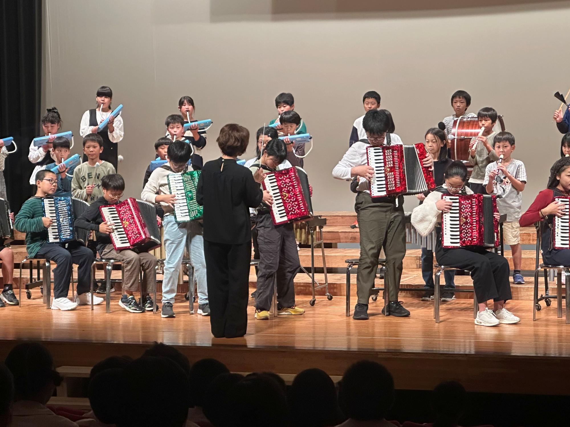 ステージで児童たちがアコーディオンや鍵盤ハーモニカを演奏している写真