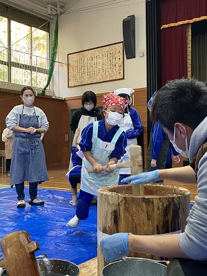 体育館で児童が杵と臼を使って餅つきを行っている写真