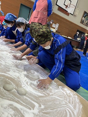 体育館で児童たちが台の上で餅の形を整えている様子の写真