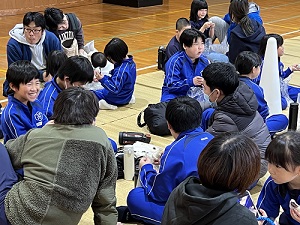体育館で児童たちや大人たちが食事を取りながら話し合いを行っている写真