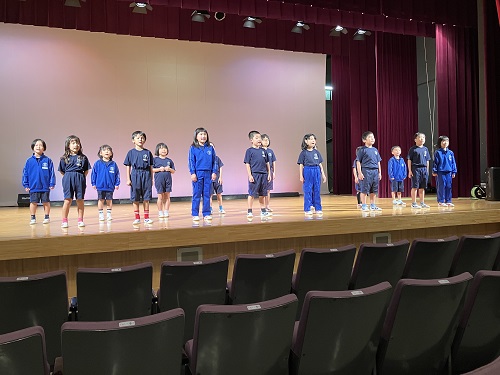 発表会で児童たちがステージに並んで歌や発表をしている写真