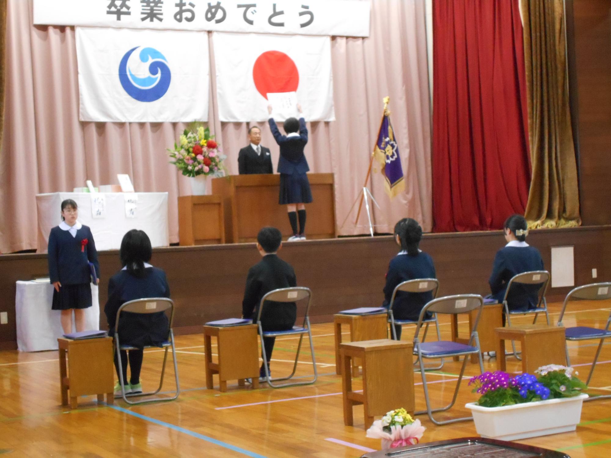体育館で児童が卒業証書を受け取っている写真