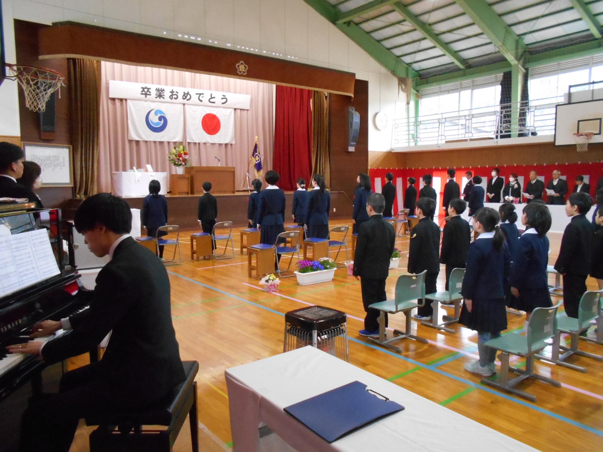 体育館で児童たちが卒業式に参加して校歌を歌唱している写真