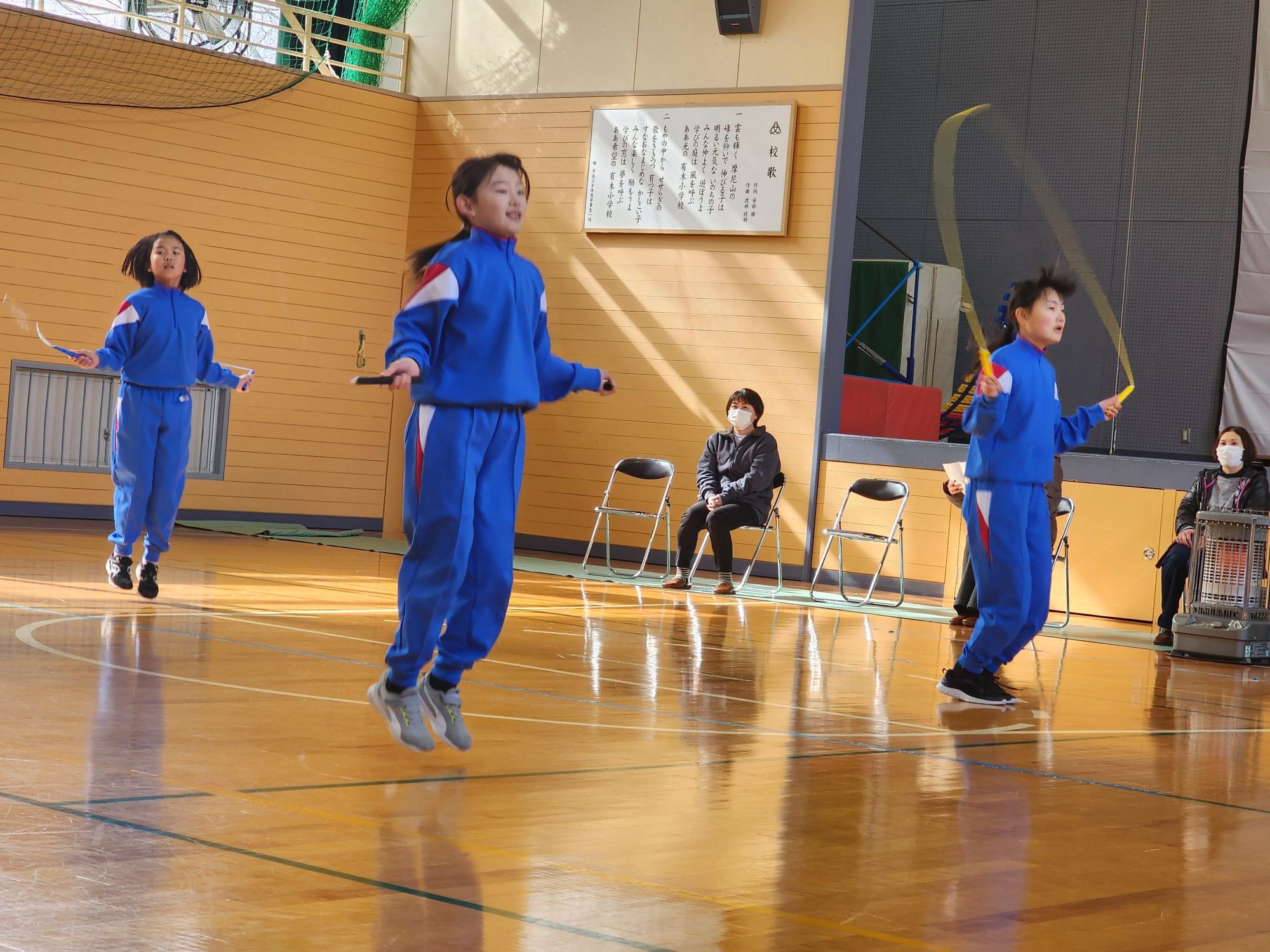 体育館で青いジャージを着た児童たちが縄跳びをしている写真