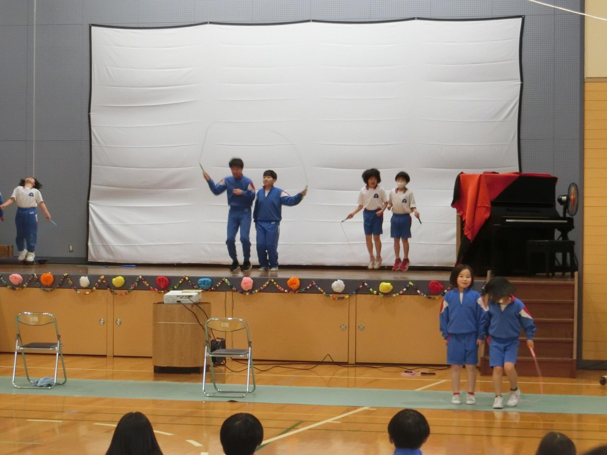 体育館の壇上で児童たちが二人組で発表をしている写真