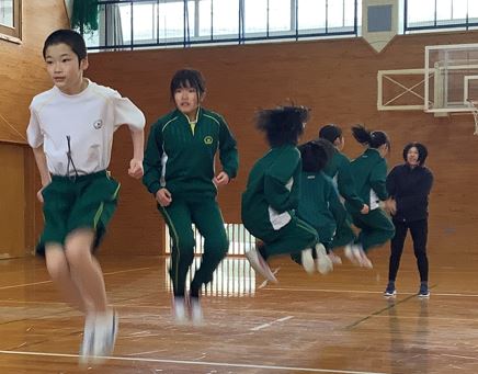体育館で児童たちが大縄跳びに挑戦している写真