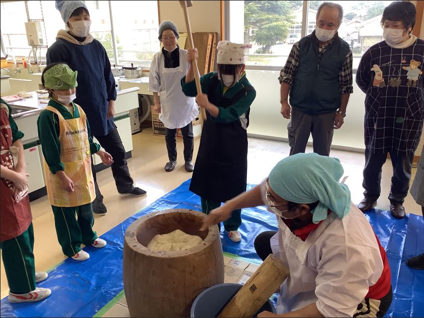 児童と地域の人たちが協力して餅つきをしている写真