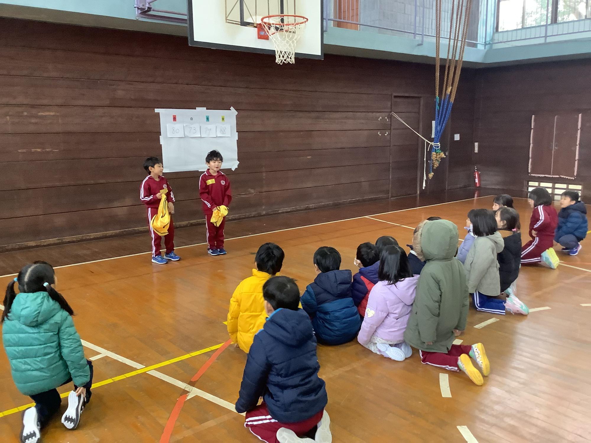 体育館で児童たちが前に立つ児童の話を聞いている写真