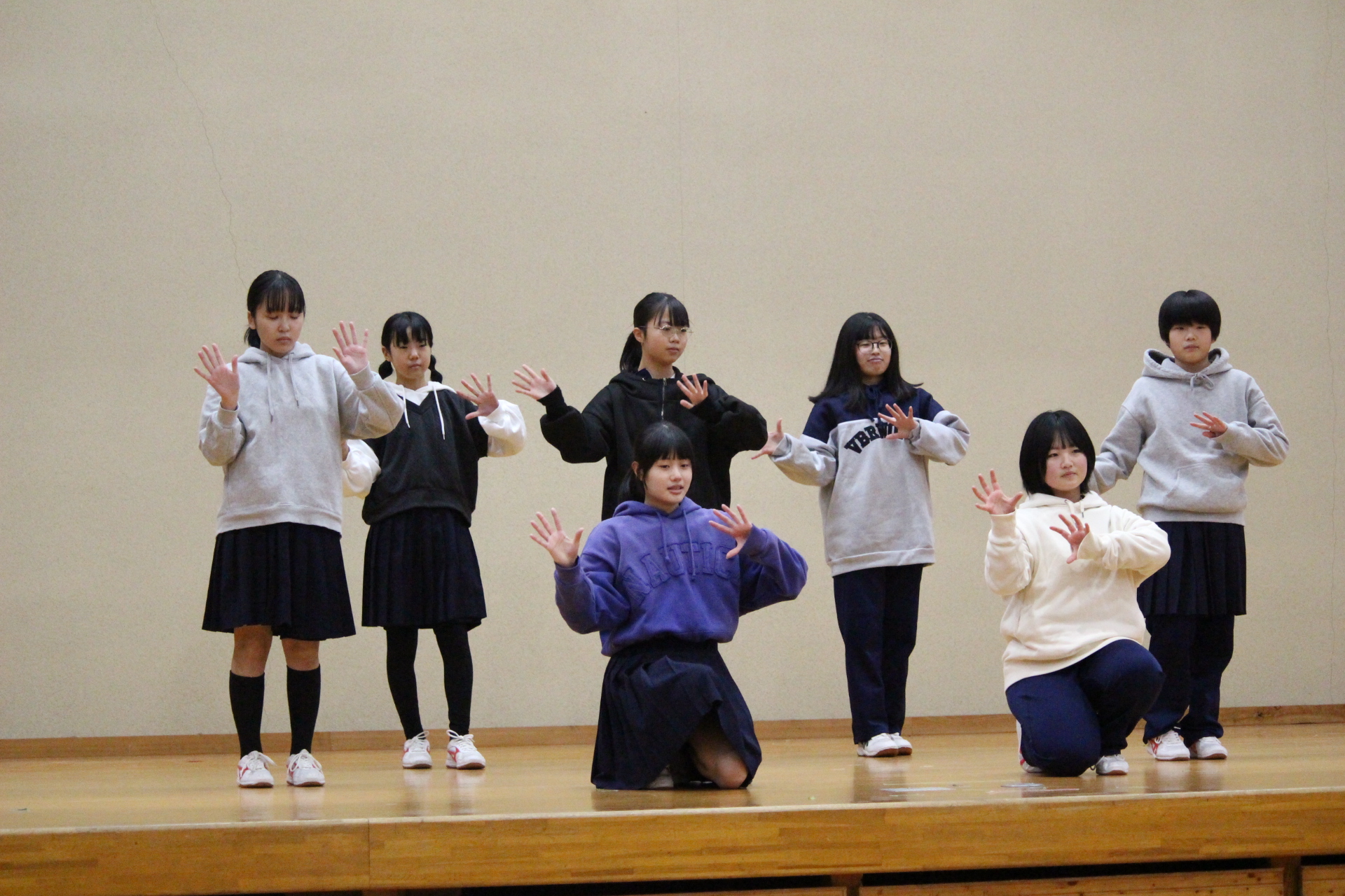 体育館の舞台で女子生徒たちがパーカー姿でダンスをしている写真