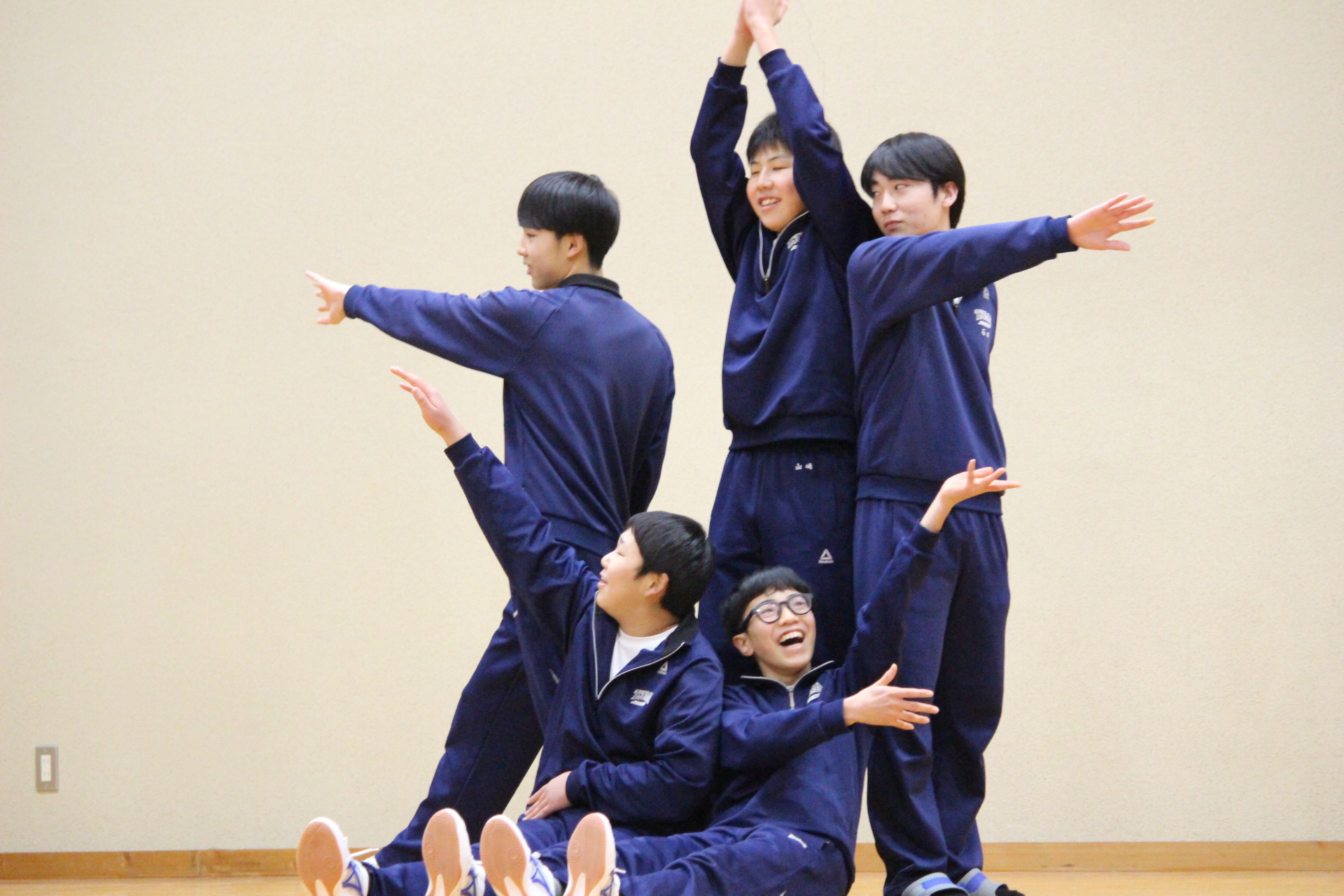 体育館の舞台で男子生徒たちがポーズを取って笑顔を見せている写真