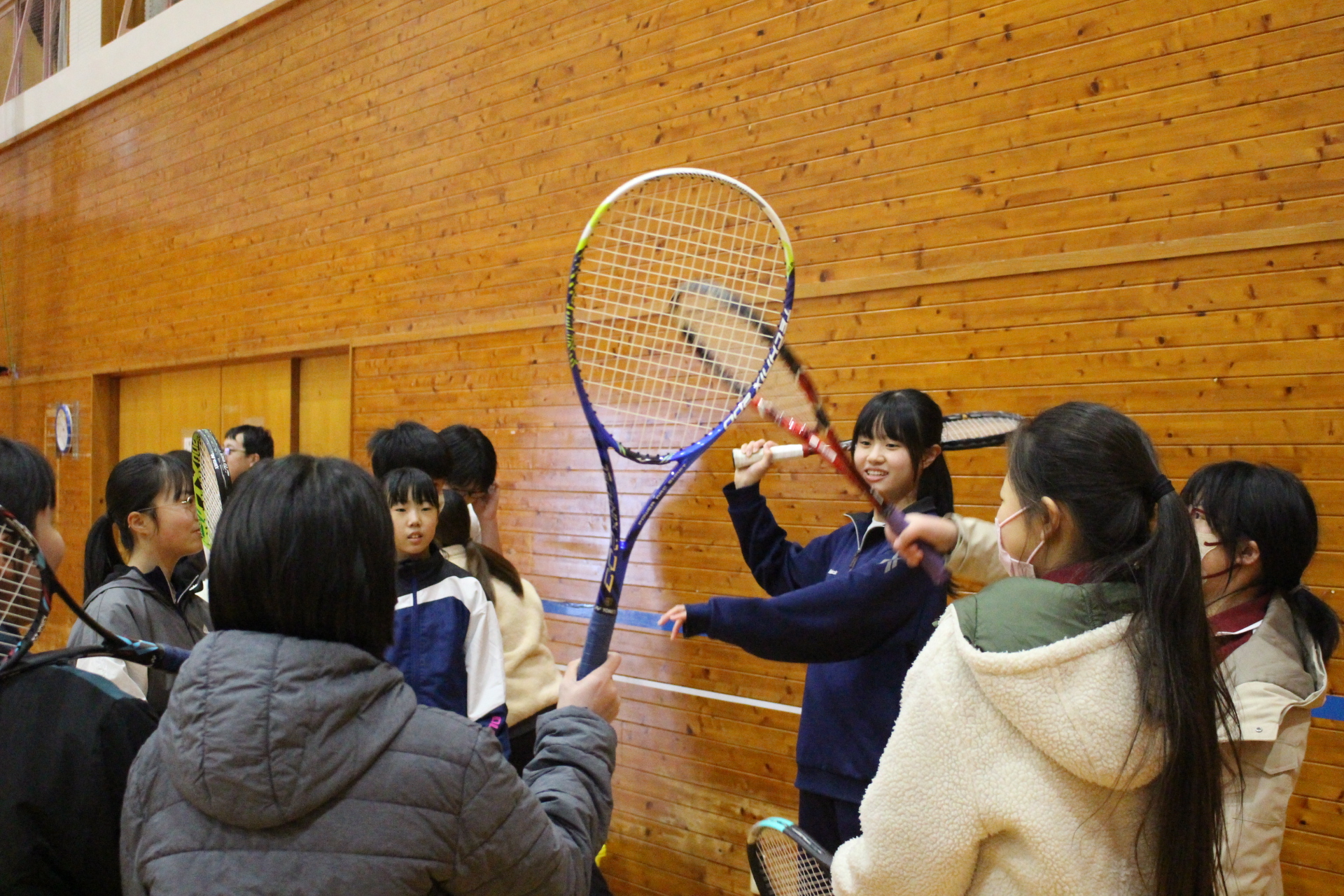 体育館で女子生徒たちがテニスラケットを掲げて円になっている写真