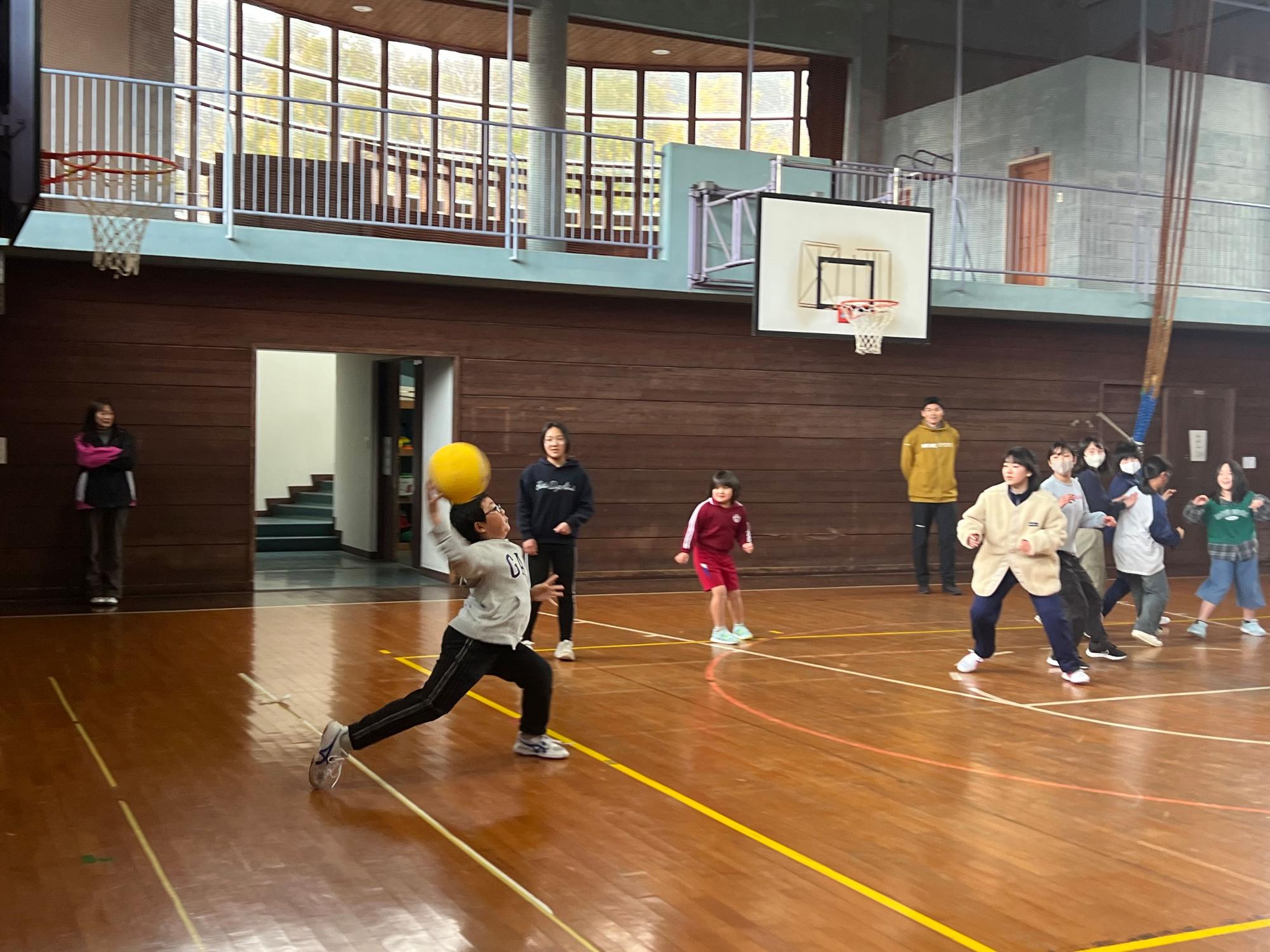 体育館で児童たちと生徒たちが黄色いボールを使ってドッジボールをしている写真