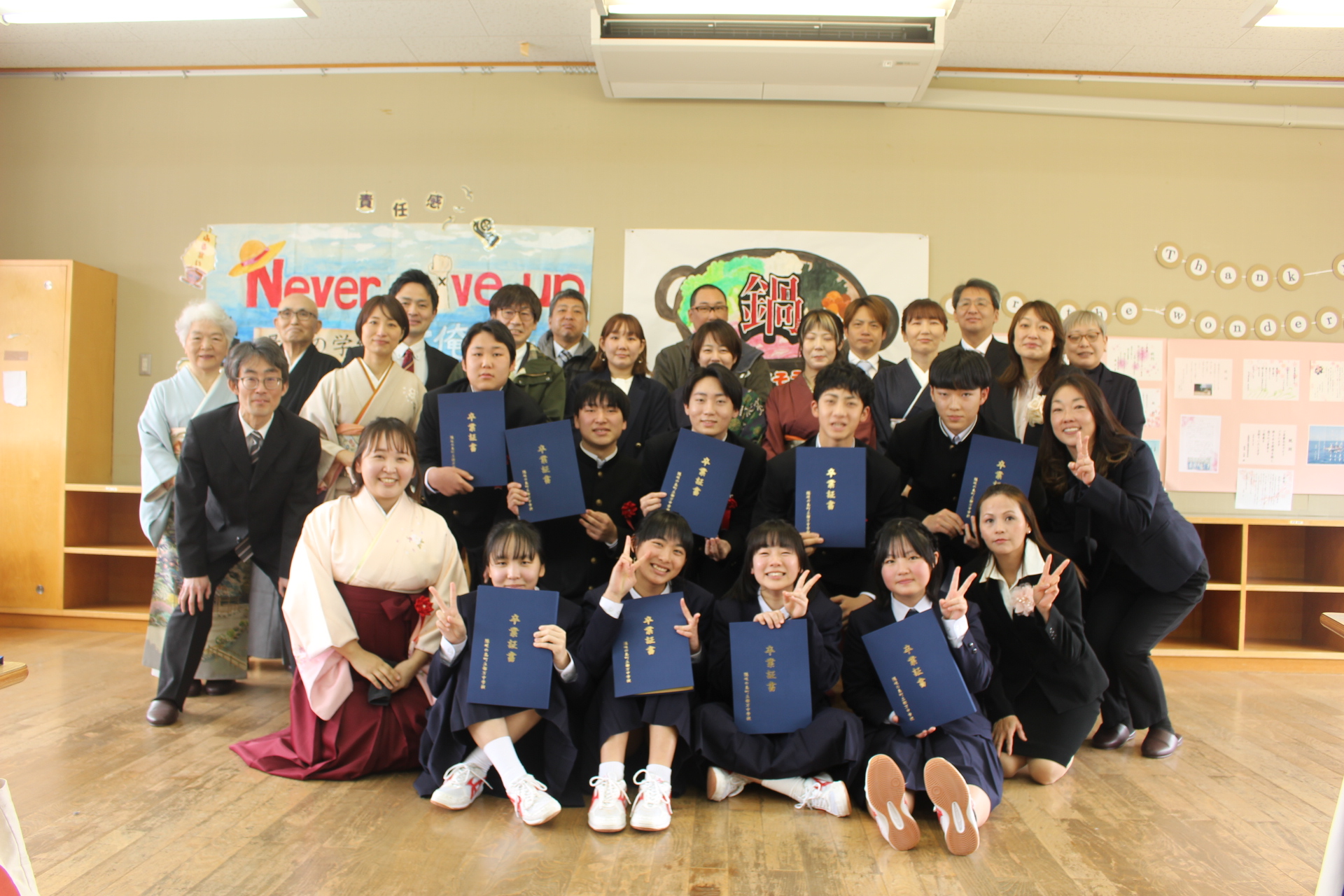 教室で卒業証書を持った生徒たちと教職員の記念写真