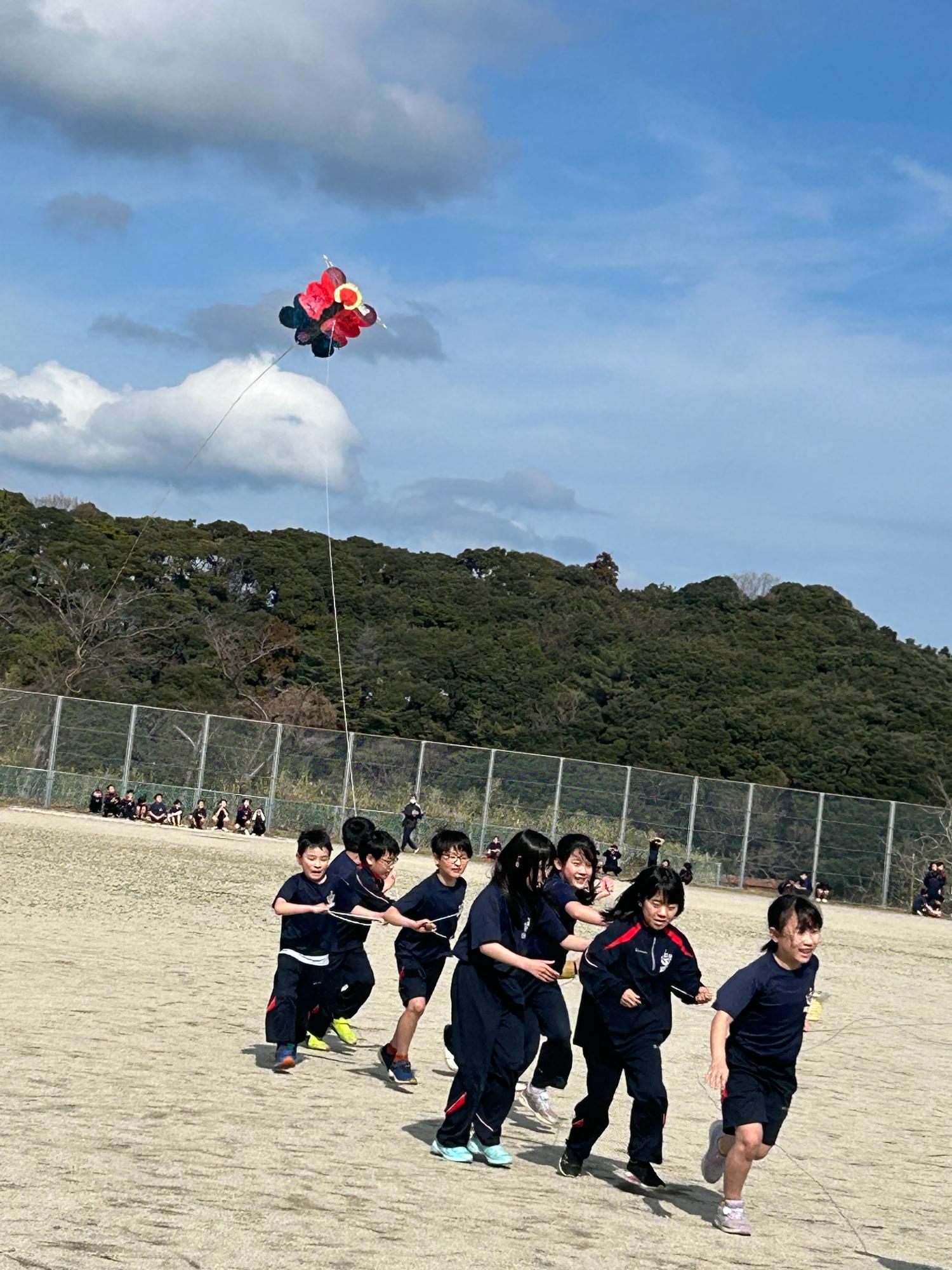 校庭で子どもたちが協力して凧を揚げている写真