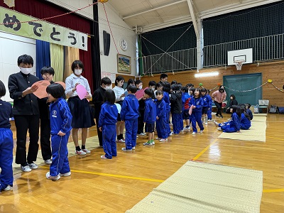 体育館で低学年の子供から6年生に一列に並び手紙を渡している写真