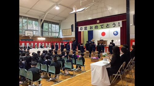 体育館で並べられたパイプ椅子に着席する児童らと舞台上で表彰式が行われている写真