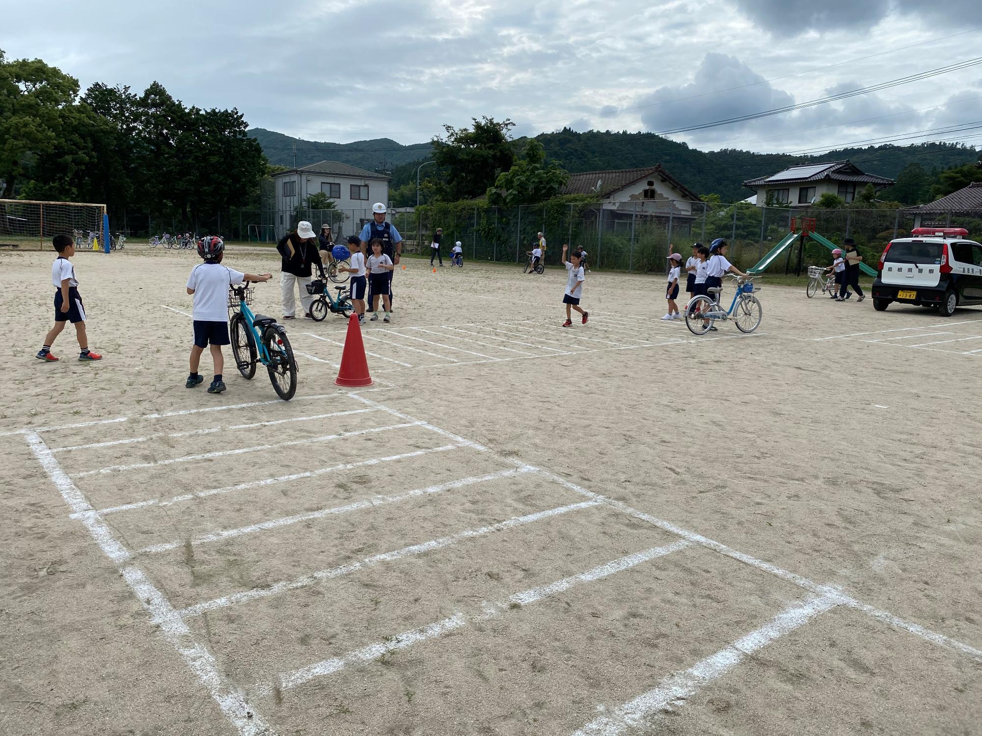 運動場で児童たちが自転車に乗って交通安全教室を受けている写真
