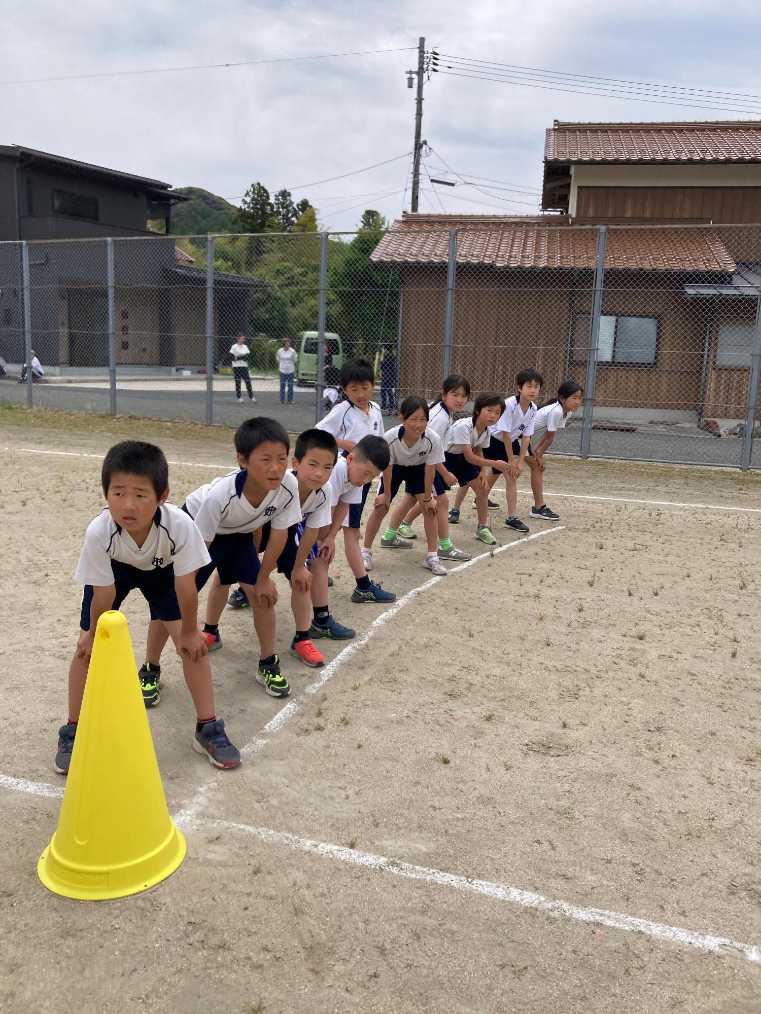 運動場で児童たちがスタートラインに並んで構えている写真