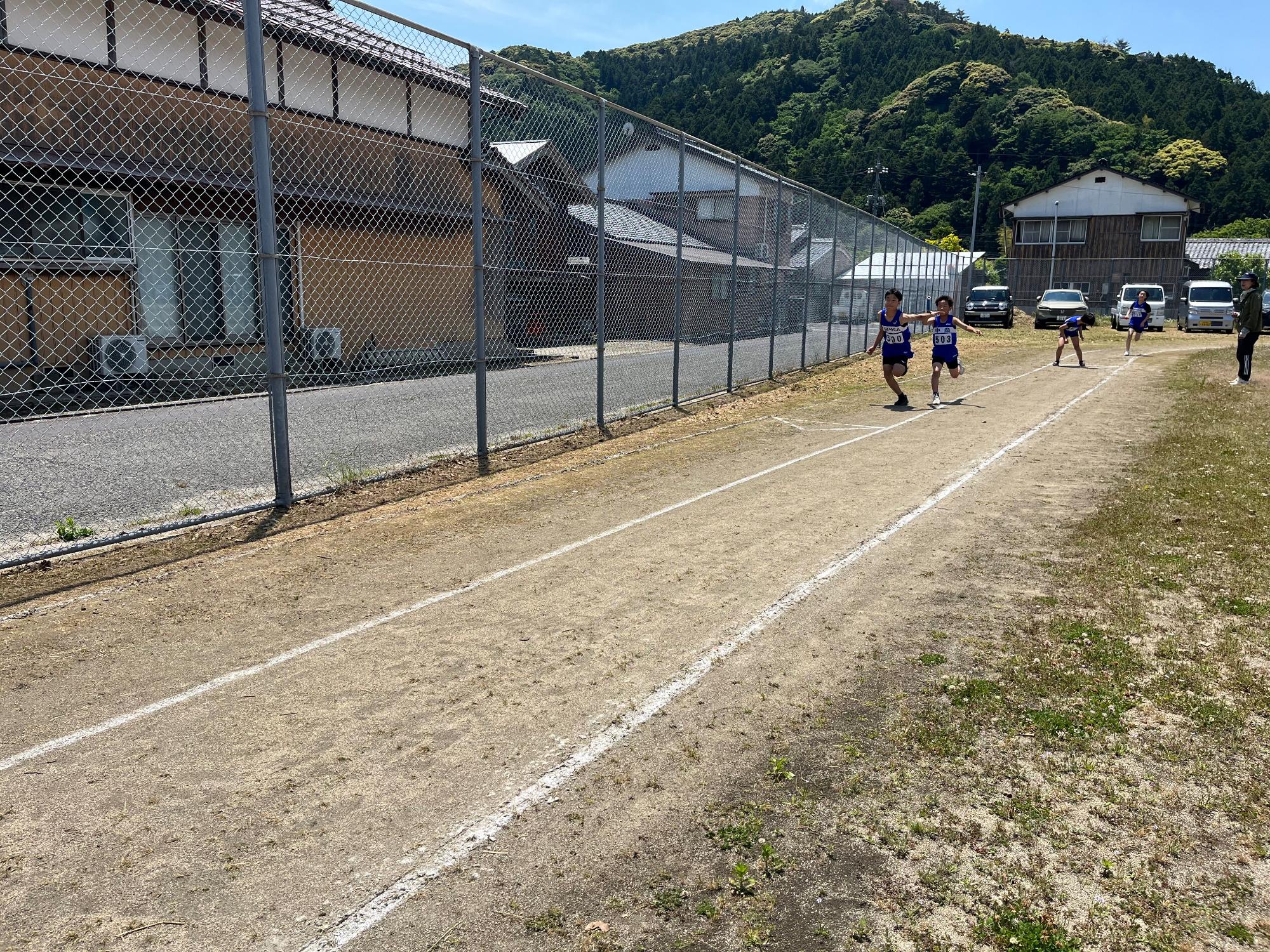 運動場で選手たちがバトンパスを行いながら走ってくる写真