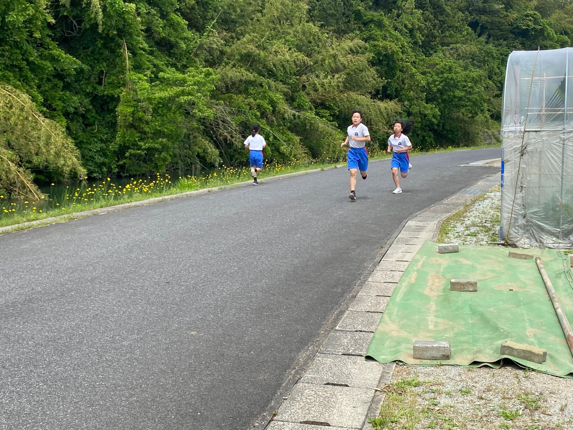 道路で体操着を着た児童たちが力いっぱい走っている写真