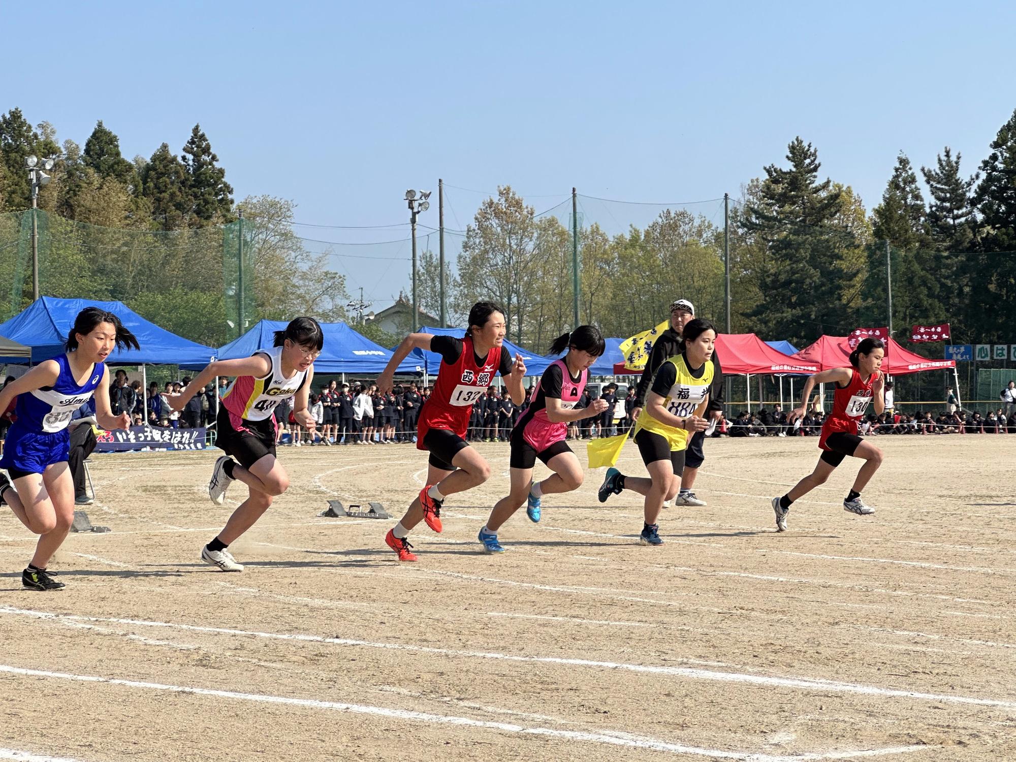 グラウンドでユニフォームを着た女子選手たちがスタートラインから一斉に走り出す陸上競技の写真