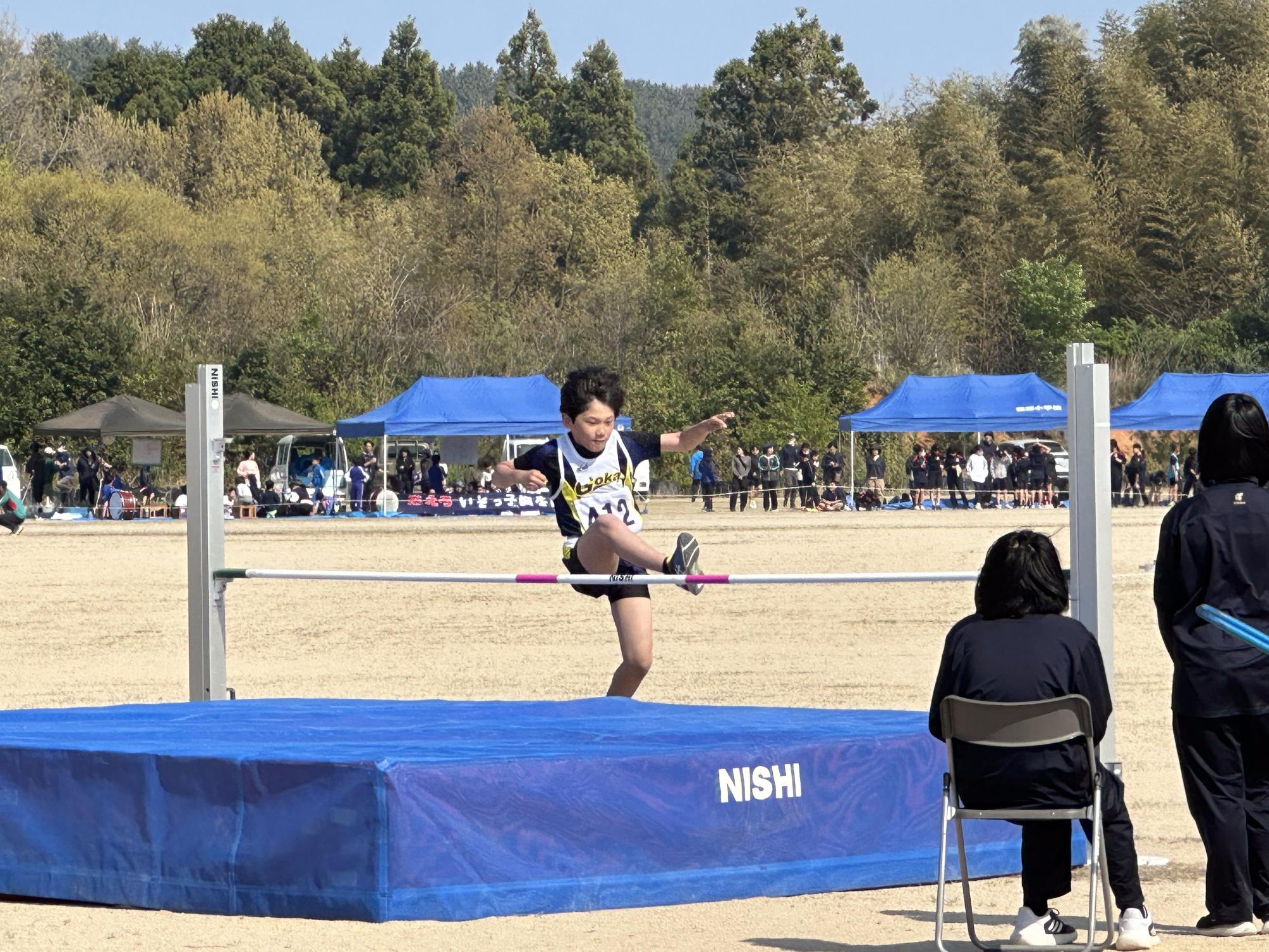 グラウンドでユニフォームを着た選手が走り高跳びのバーを跳び越えている写真