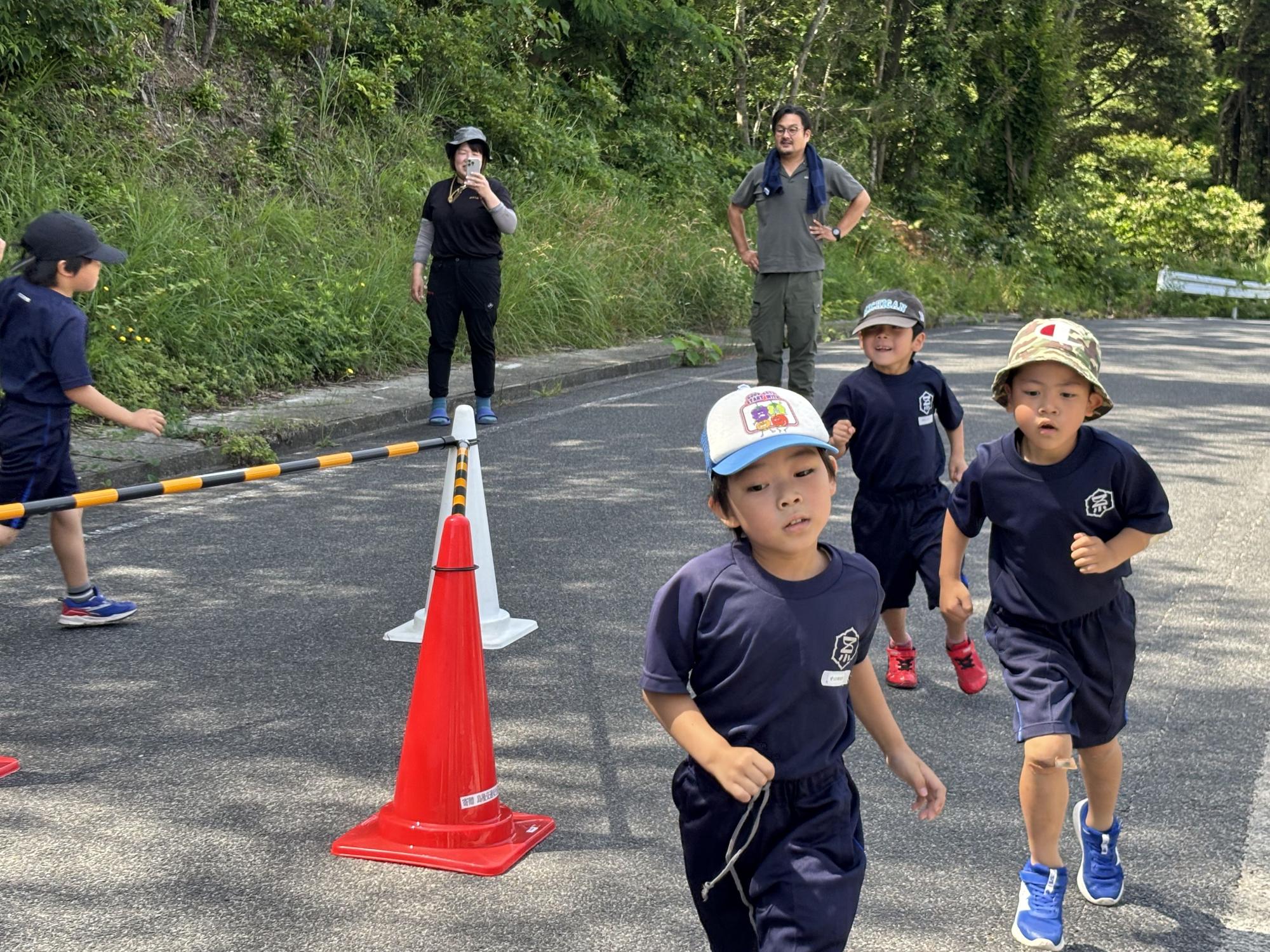 屋外の道路で体操服を着た児童たちがコーンの間を走り抜けている写真