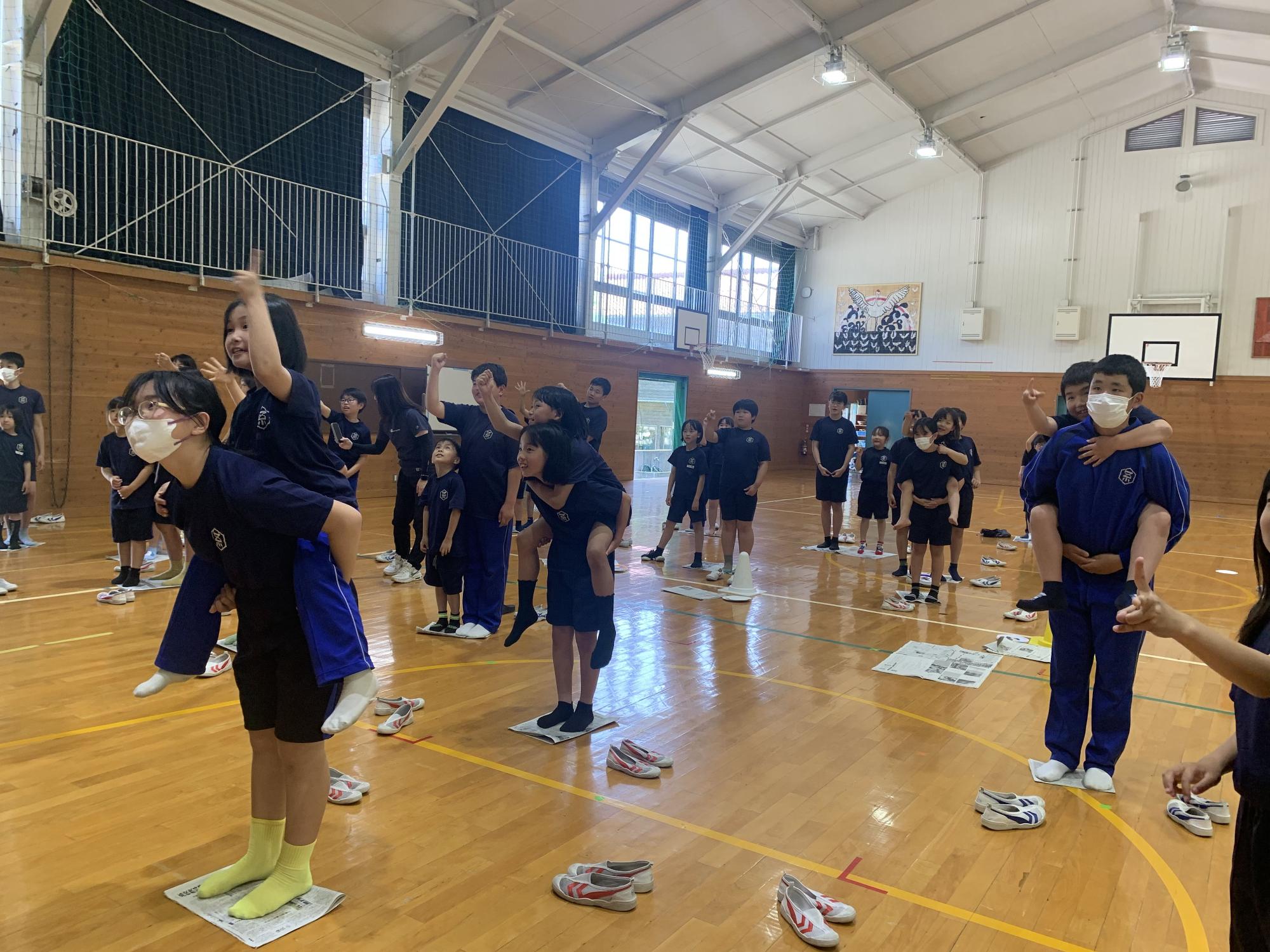 体育館で児童たちがペアになっておんぶをしながらゲームをしている写真