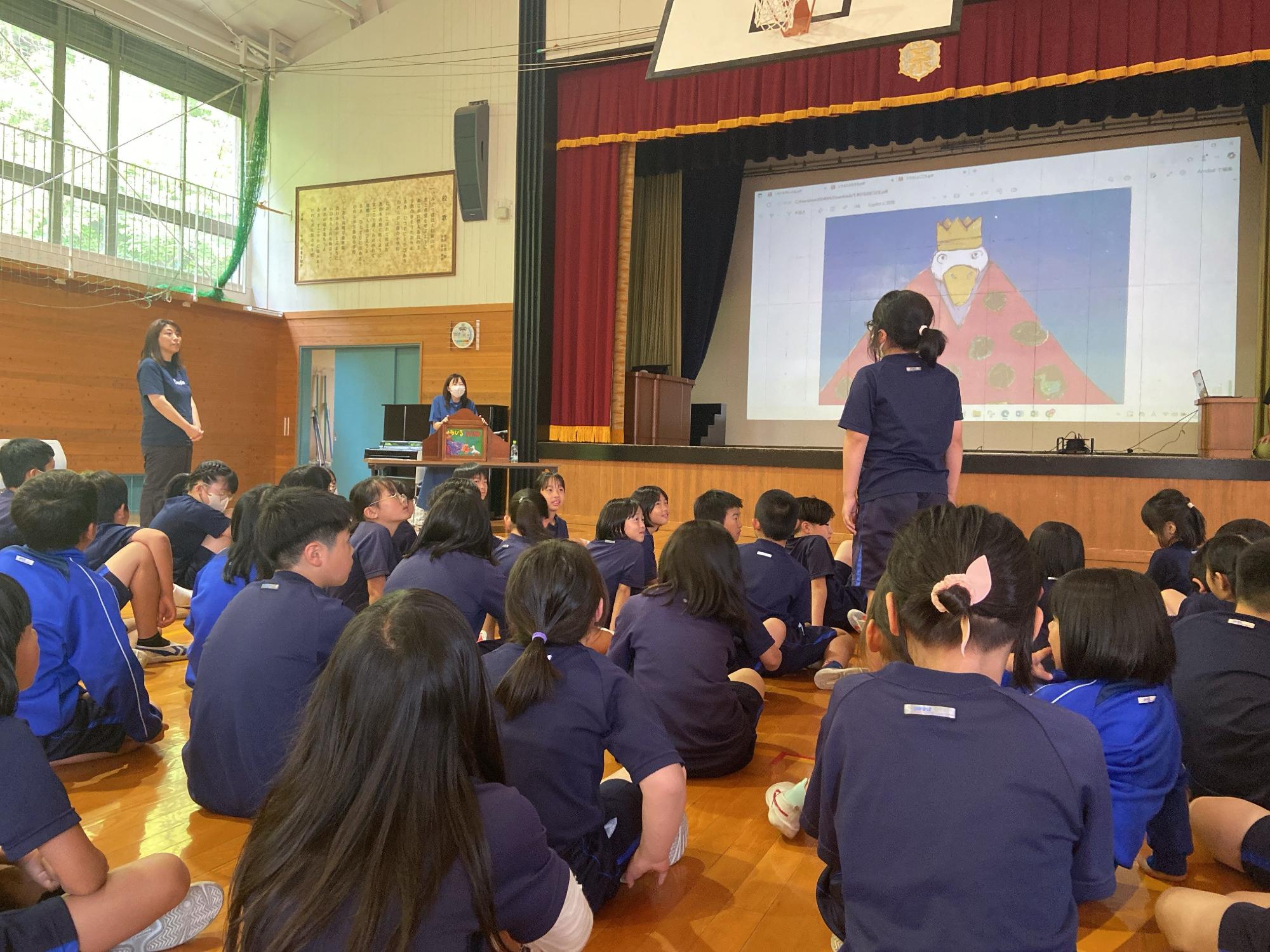 体育館でたくさんの児童たちが座って紙芝居の発表を見ている写真