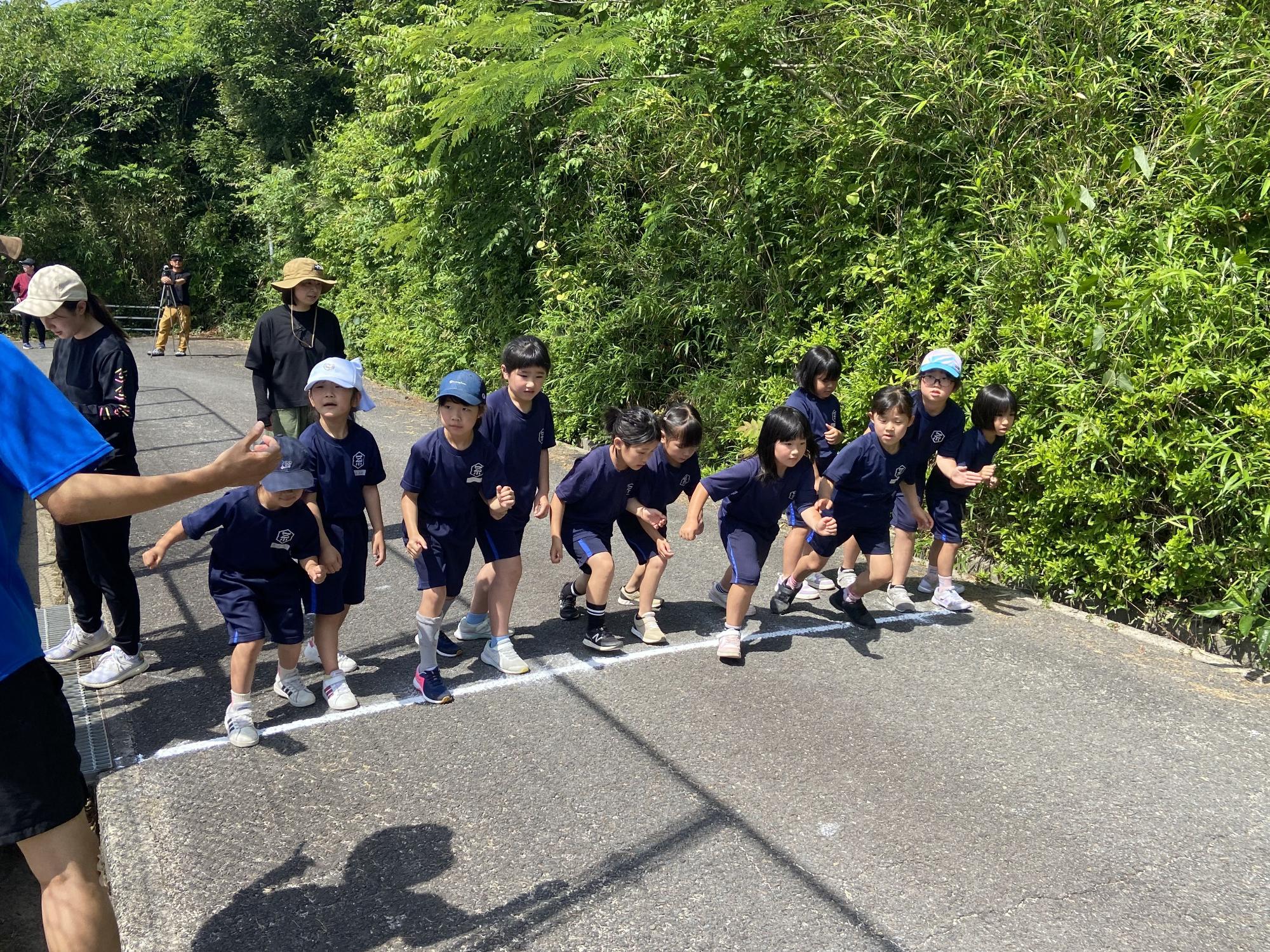 屋外の道路で体操服を着た児童たちがスタートラインに並び、構えている写真